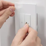 Elektryk pokazuje, jak podłączyć włącznik dotykowy LED. Widać adapter LED i kable L (faza) oraz L1 (wyjście) przy szklanym włączniku.